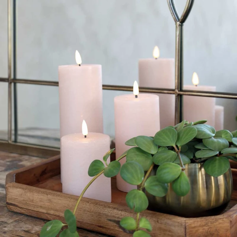Drei Chic Antique – Stumpenkerze LED staubig rosa inkl. Batterie auf einem Holztablett mit einer Topfpflanze vor einem Spiegel, der das Arrangement reflektiert.