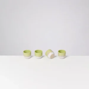 Vier grüne Teetassen auf einem weißen Tisch, eine davon liegt seitlich.