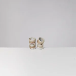 Vier stapelbare, beige-weiße Keramikbecher auf weißem Tisch, minimalistisch vor grauem Hintergrund.