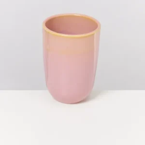 Rosa Vase aus Keramik steht auf einer weißen Oberfläche vor einem grauen Hintergrund.