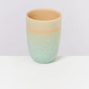Keramikbecher mit pastellgrüner und beiger Glasur steht auf weißem Hintergrund.