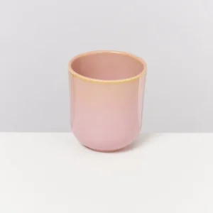 Ein rosa Keramikbecher mit leichtem Gelbton auf einem weißen Hintergrund.