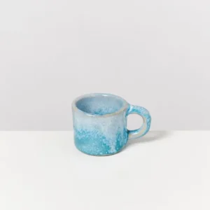 Eine kleine, blaue Keramiktasse mit Henkel steht auf einem weißen Hintergrund.