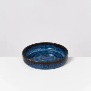 Runde, blaue Keramikschale mit dunklen Rändern auf weißem Hintergrund.