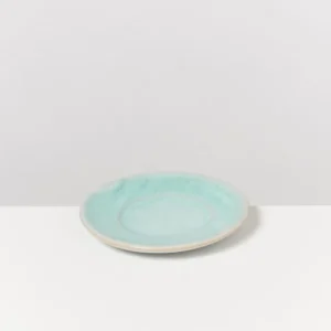 Ein blauer Keramikteller mit hellerem Rand steht auf einem weißen Tisch vor einem grauen Hintergrund.