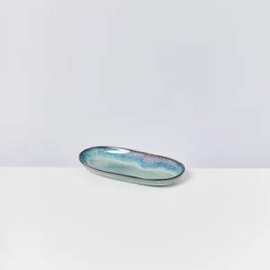Langes, ovales Keramikschälchen in Blau- und Grüntönen auf einem weißen Tisch vor neutralem Hintergrund.