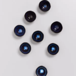 Acht blaue Keramikschalen liegen auf einem weißen Hintergrund in lockerer Anordnung.