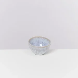 Kleine, hellblaue Keramikschale mit braunem Rand auf einem weißen Untergrund vor grauem Hintergrund.